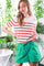 woman wearing a cream striped sweater with red stripes and green high-waisted shorts, posing in a vibrant indoor setting