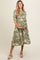 woman wearing a floral green maternity dress with a collared neck and short sleeves, holding her baby bump