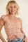 woman wearing a floral smocked tank top with ruffled sleeves and a drawstring detail, smiling at the camera