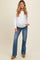 woman wearing a white long sleeve maternity top and blue flared jeans, showing her baby bump