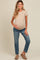 woman wearing a beige maternity t-shirt and blue jeans, holding her baby bump with one hand