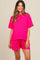 woman wearing a bright pink ribbed short sleeve maternity top and matching shorts, smiling at the camera