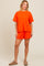woman wearing an orange striped short-sleeve top and matching shorts, standing in a casual pose
