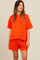 woman wearing a bright orange striped maternity top and matching shorts, smiling against a neutral background
