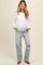 woman wearing a white long sleeve maternity top with a baby bump and distressed light wash jeans