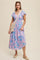 woman wearing a pink and blue floral patterned maxi dress with short flutter sleeves and a braided bag
