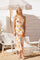woman wearing a floral midi dress with orange and yellow flowers, standing under a beach umbrella