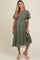 woman wearing a green maternity dress with short puff sleeves and floral lace details, holding the hem of the dress