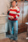 woman wearing a red and white striped maternity polo sweater and light blue flared jeans, holding her baby bump