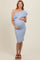 woman wearing a light blue one-shoulder maternity dress with ruffle detail and holding her baby bump