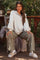 woman wearing a light gray maternity pullover with sleeves and green checkered maternity pants, sitting on a porch