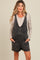 woman wearing a black denim maternity overall with front pockets and a beige button-up long sleeve top underneath