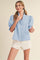 woman wearing a light blue puff sleeve blouse with ruffle detailing paired with white shorts
