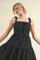 woman wearing a black tiered midi dress with bow detail on the bodice and adjustable straps