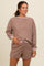 woman wearing a brown checkered maternity loungewear set with a long sleeve top and matching shorts, holding her baby bump