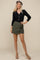 woman wearing a black ribbed cardigan with buttons and olive green wrap shorts, accessorized with a leopard print beret
