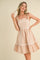 woman wearing a blush pink sleeveless dress with white trim and ruffled hem, holding a lock of hair