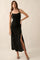 woman wearing a black maxi dress with scalloped edges and side slits, styled with strappy heels