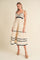 woman wearing a cream sleeveless tiered maxi dress with black scalloped details and shoulder ties