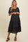 woman wearing a black floral maternity dress with short puff sleeves and a flowy skirt, standing and smiling