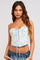 woman wearing a white floral corset top with blue accents and lace-up front, paired with denim jeans