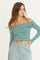 woman wearing a green and white striped off-the-shoulder crop top with long sleeves and gray tailored pants