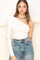 woman wearing a white one-shoulder fitted top with a long sleeve, paired with high-waisted denim jeans