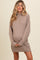 woman wearing a cozy beige maternity sweater dress with oversized sleeves and ribbed detailing, holding her baby bump