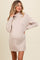 woman wearing a beige maternity sweater dress with a cowl neck and ribbed hem, showing her baby bump