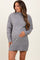 woman wearing a gray maternity sweater dress with a high neck and ribbed hem, gently cradling her baby bump