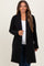 woman wearing a black maternity duster coat over a white top and jeans, smiling at the camera