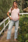 woman wearing a pink maternity t-shirt and distressed light blue maternity jeans, showcasing her baby bump outdoors