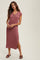woman wearing a mauve ribbed midi dress with short sleeves and buttons, standing with hands clasped in front