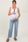 woman wearing a white tank top and light blue jeans, showing her baby bump while holding it gently
