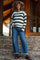 woman wearing a black and white striped maternity sweater and wide-leg jeans, holding her baby bump on a stone staircase