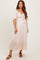 woman wearing a light beige maternity dress with a ruched bodice and puff sleeves, standing against a neutral background