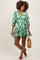 woman wearing a green floral maternity dress with a v-neck and balloon sleeves, holding a woven bag and showing her baby bump