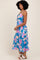 woman wearing a blue floral maxi dress with a tie detail and spaghetti straps, styled with white sandals