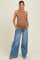 woman wearing a brown ribbed maternity tank top and wide-leg light blue jeans, cradling her baby bump