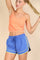 woman wearing a bright orange cropped tank top and blue athletic shorts with yellow trim