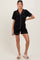 woman wearing a black maternity pajama set with short sleeves and shorts, featuring white piping details