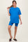 woman wearing a bright blue maternity oversized t-shirt and matching blue bike shorts, holding her hair up with one hand