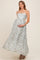 woman wearing a light green floral maternity maxi dress with cutout sides and a scalloped hem, holding her baby bump