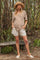 woman wearing a striped brown maternity top and beige shorts, standing outdoors with a straw hat