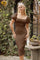 woman wearing a brown square neck fitted dress with puff sleeves, posing outdoors in a leafy setting