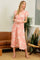 woman wearing a pink floral maxi dress with short ruffled sleeves and a cinched waist, standing in a bright indoor setting