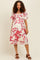 woman wearing a white floral maternity dress with short sleeves and a smocked bodice, no visible baby bump