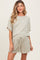 woman wearing a light beige short sleeve maternity top and matching shorts with a drawstring waist