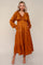 woman wearing an amber long sleeve maxi dress with a tiered design and pockets, standing on a neutral background