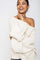 woman wearing an off-the-shoulder cream knit sweater with oversized sleeves and a cheerful expression